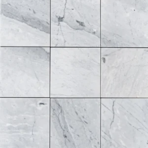 Top-down view of multiple Carrara 6"x6" honed marble tiles with soft white surface and natural gray veining in a grid layout.