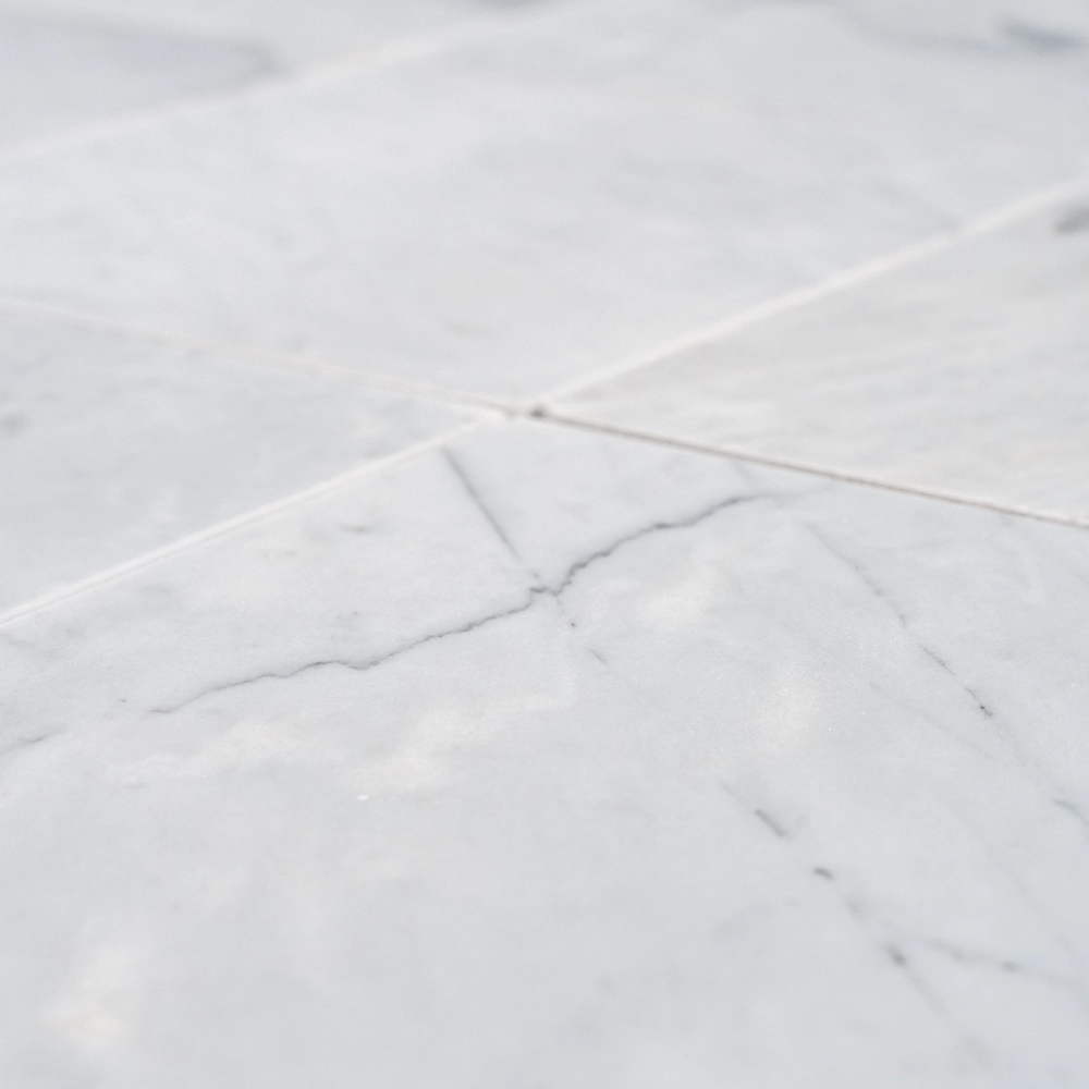 Single Carrara 6"x6" honed marble tile with crisp edges and cloudy gray veining on a light background.