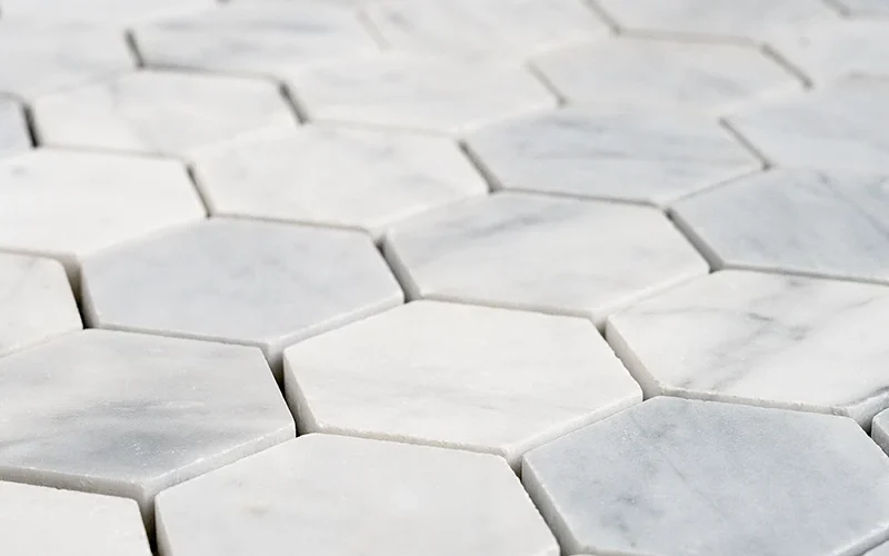 Close-up of 2-inch honed Carrara White marble honeycomb mosaic tiles with hexagon shape and soft matte finish.